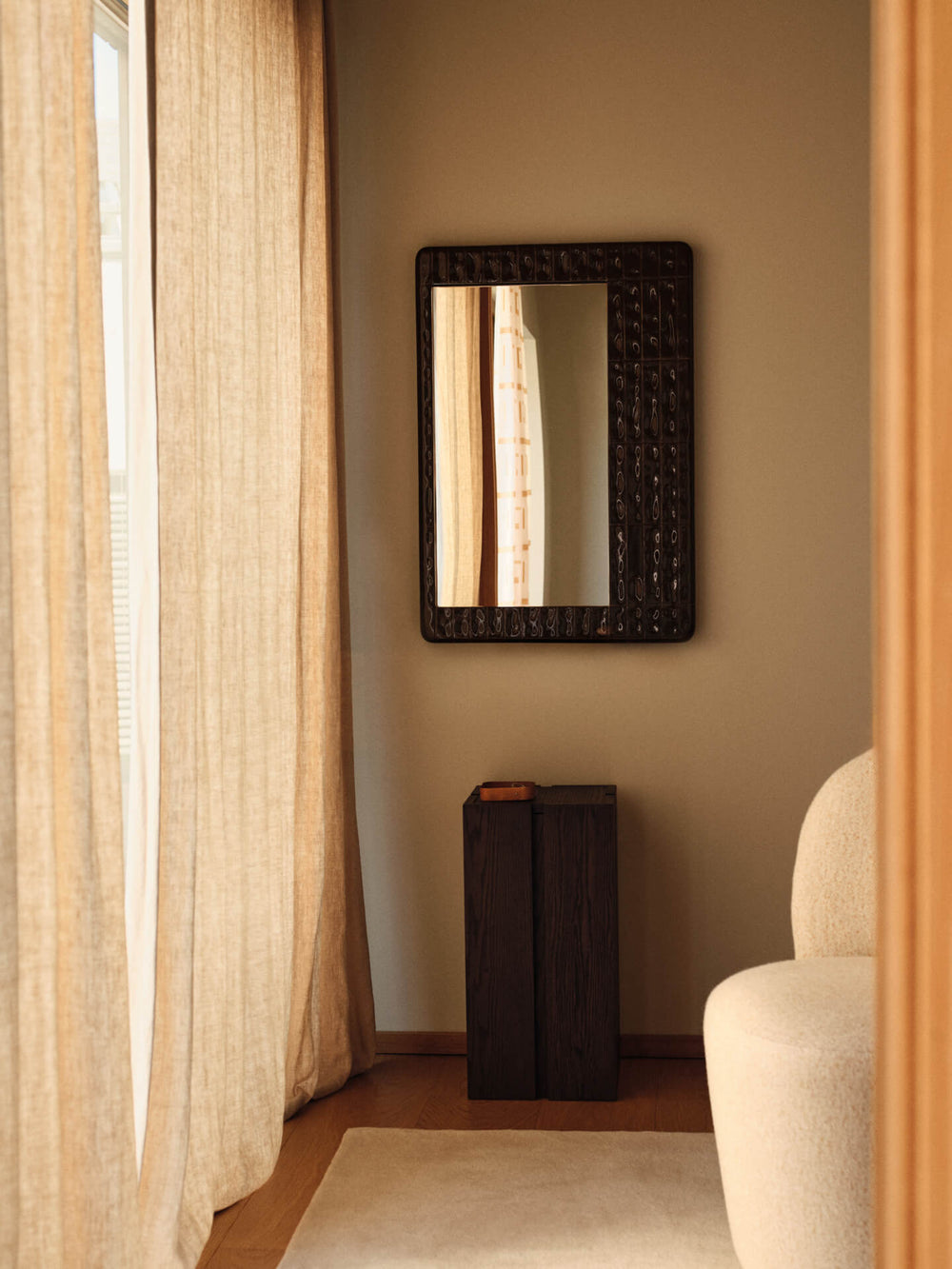 Off-white runner in a sunlit corner with a textured dark mirror, slim console and bouclé chair