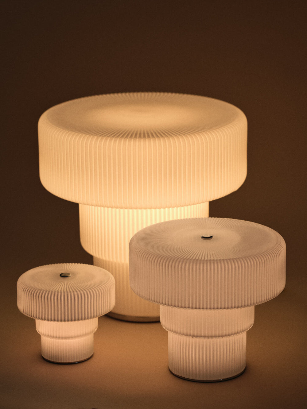 Three lit ribbed portable lamps in white, shown in three sizes side by side