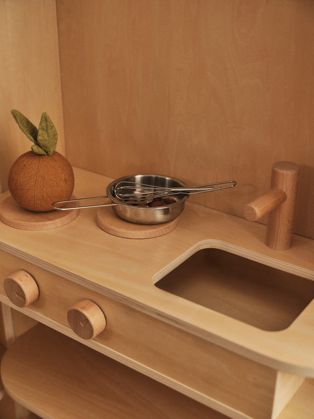 Soft orange with green leaves on a play kitchen counter beside a toy pan and whisk