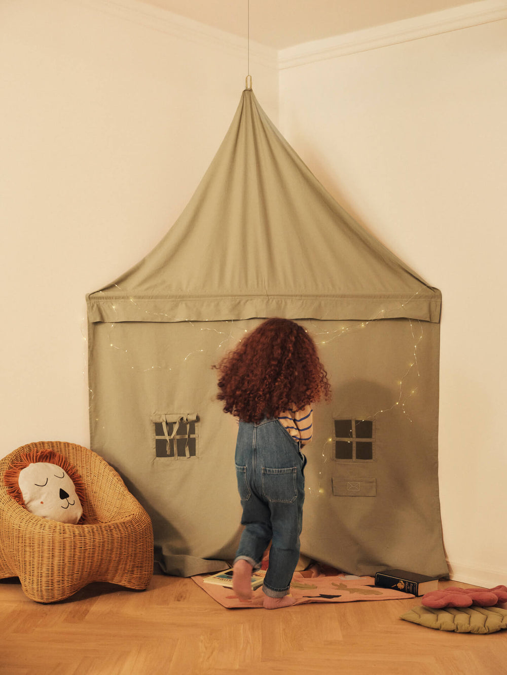 Child stepping into the corner play curtain, string lights and a lion cushion nearby