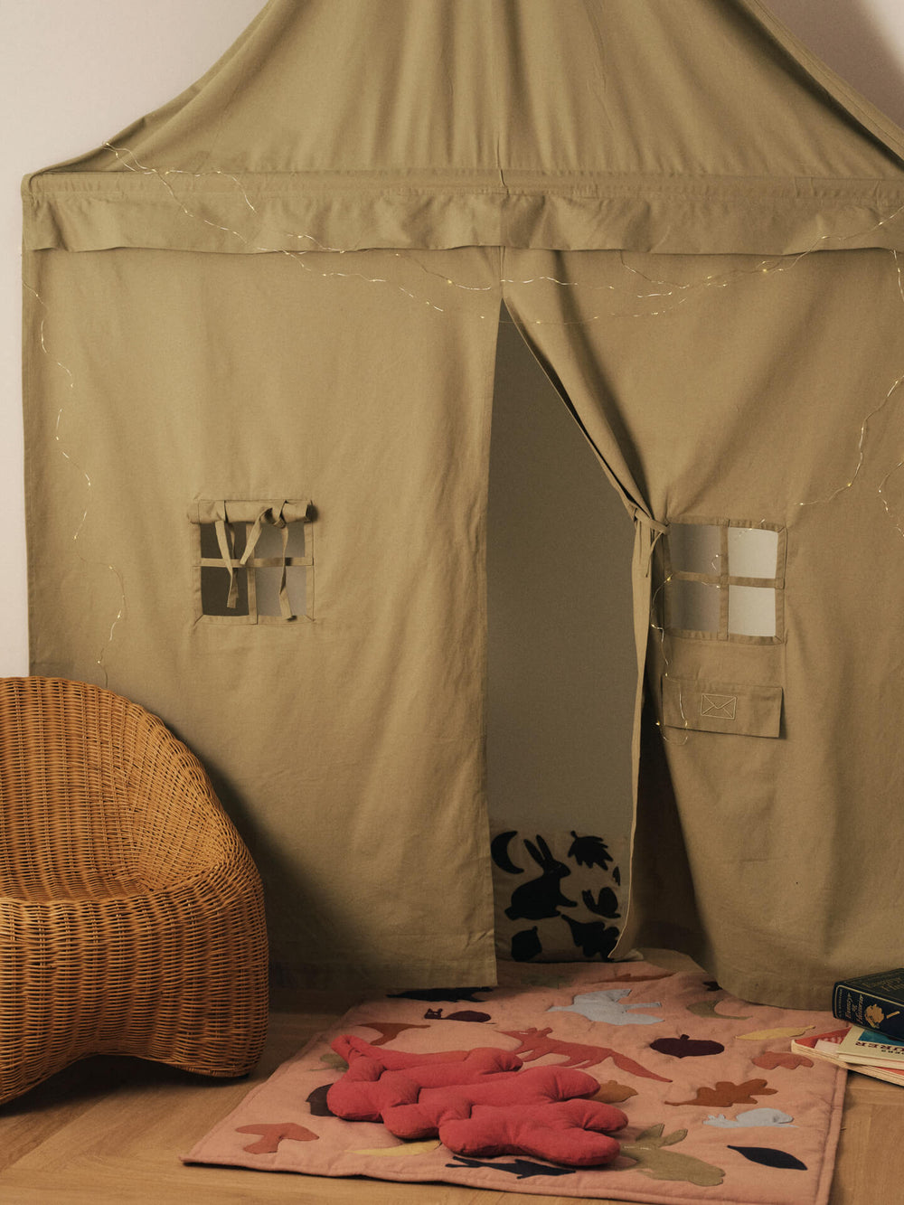 Play corner curtain hung in a room corner with fairy lights, woven chair and animal-print play mat