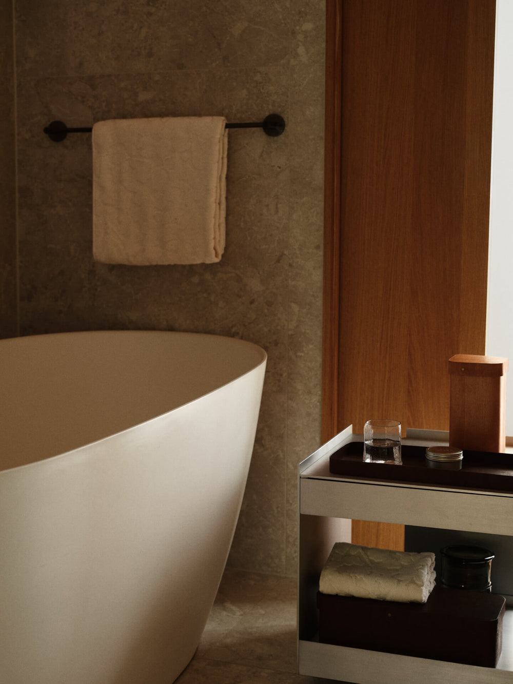 Bathroom with a freestanding tub, the off-white towel folded on a trolley shelf beside a tray and jar