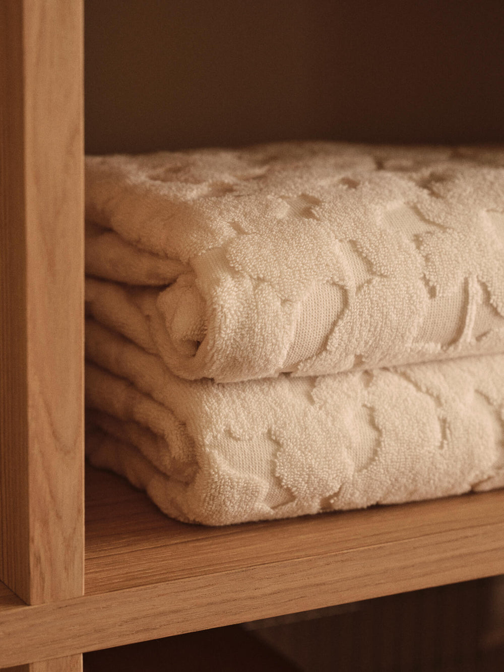 Two folded off-white towels stacked on a shelf, raised floral relief in close-up