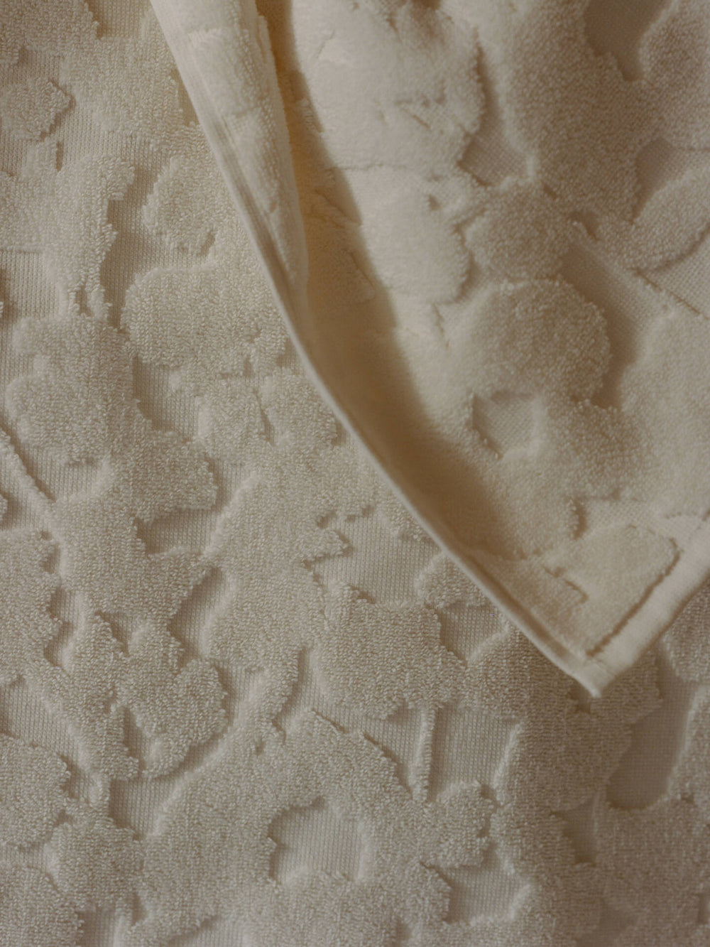 Close-up of the raised tonal floral relief and hemmed edge of the off-white towel
