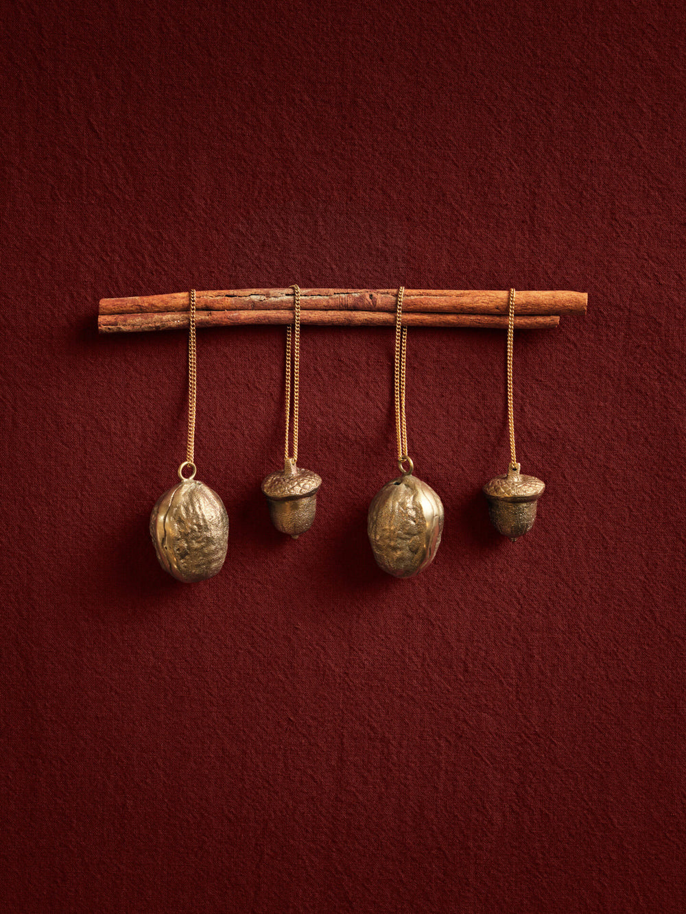 Four acorn and nut-shaped ornaments hanging on chains from sticks against a red wall