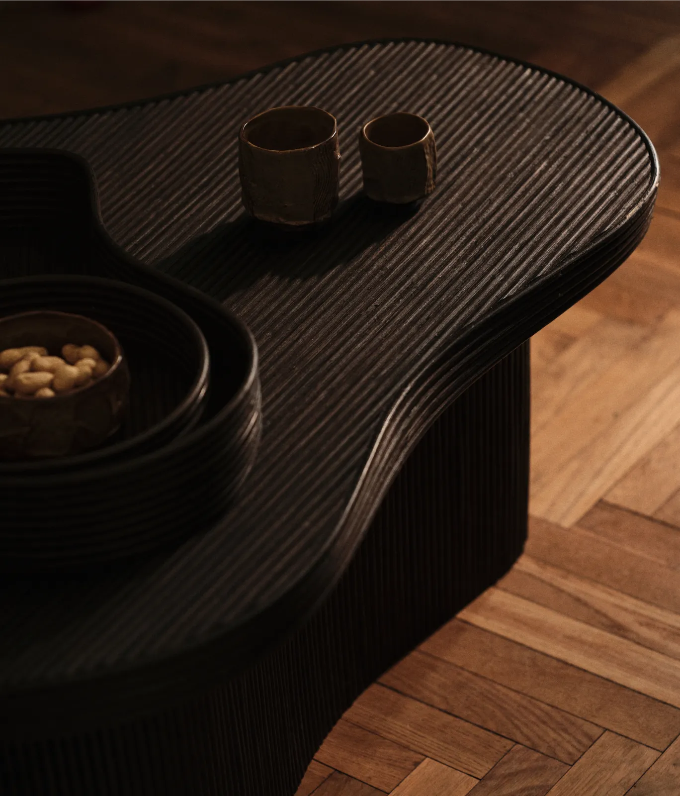 Autumn Winter 2026 collection, dark ribbed curved coffee table with two cups and a bowl of nuts