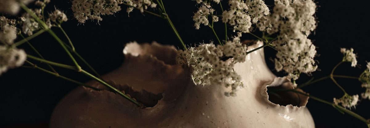 Accessories collection, close-up of an off-white vase with torn openings holding small white flowers
