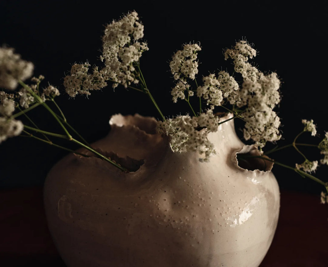 Accessories collection, close-up of an off-white vase with torn openings holding small white flowers