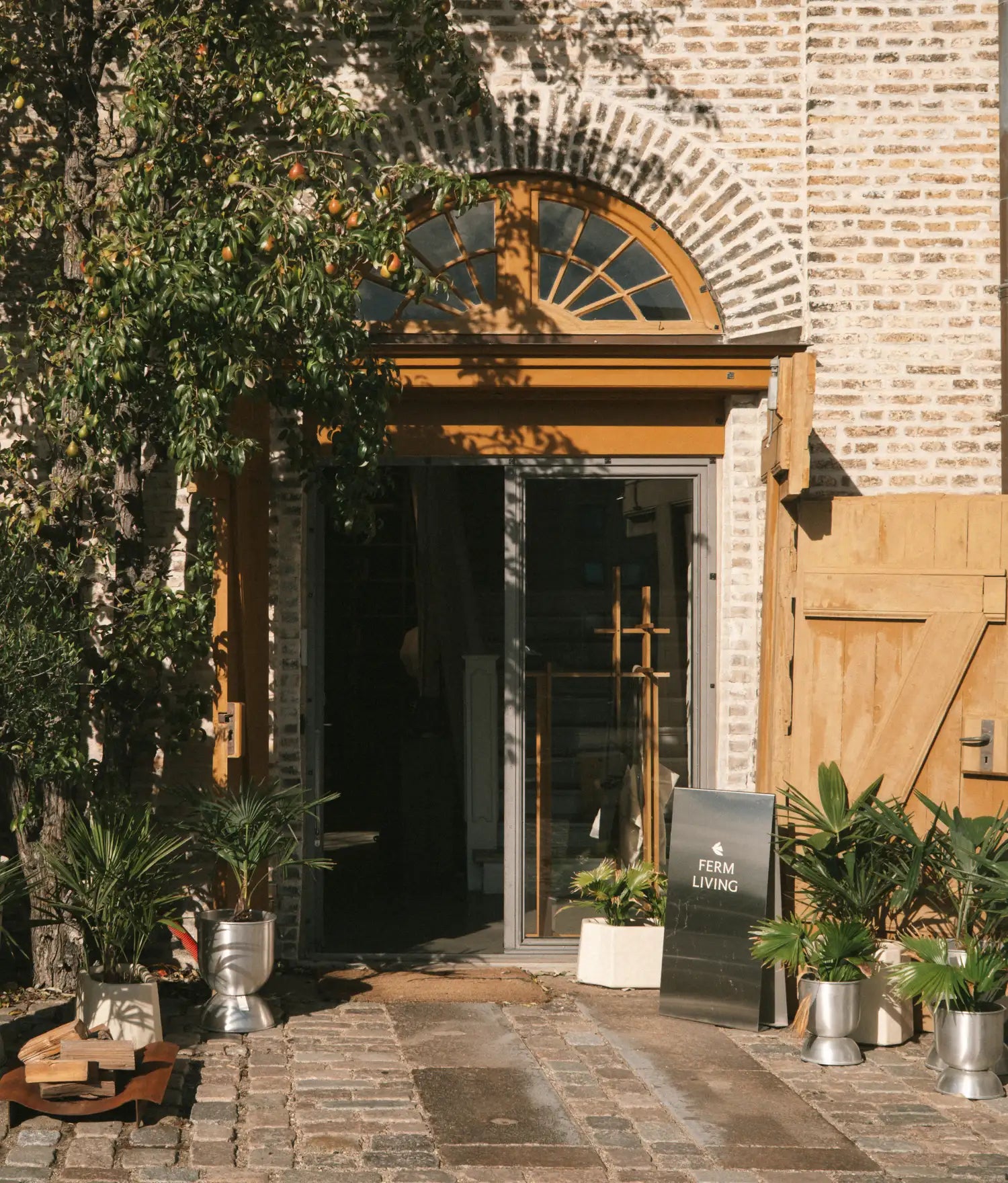 Arched brick entrance with open doors, plants in tall planters and a pavement sign